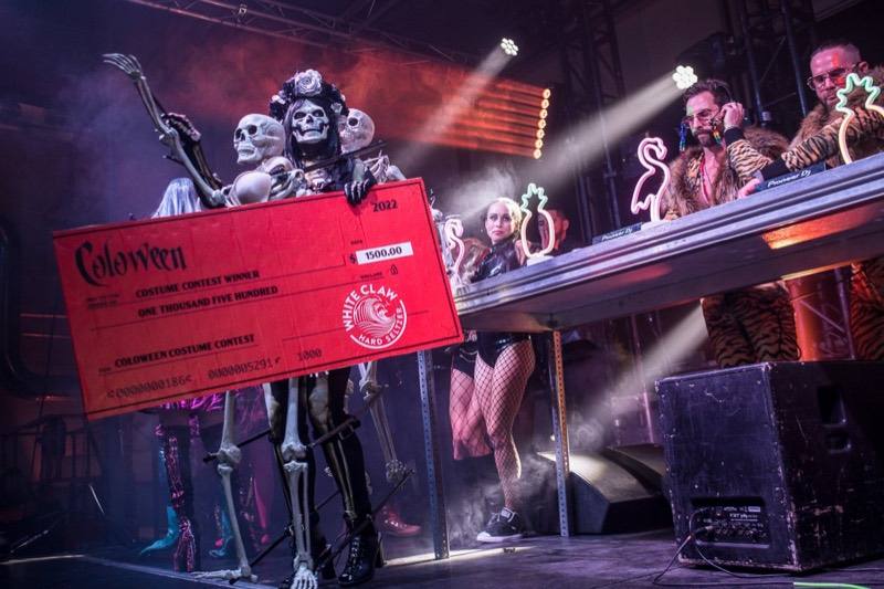 Skeleton-draped winner hoisting the giant costume contest check onstage at Coloween — Denver Halloween nightlife