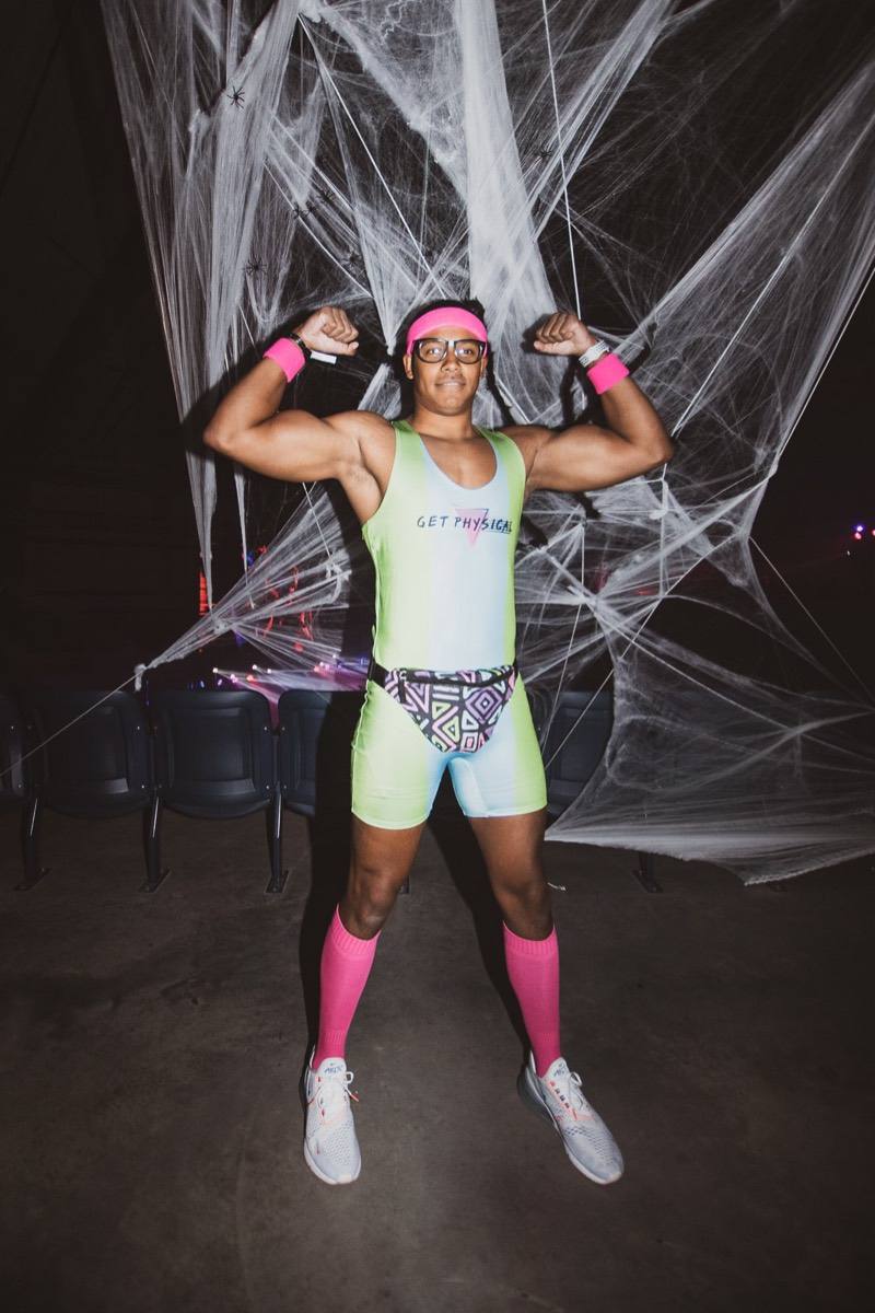 Neon 80s workout guy flexing in front of giant cobwebs at Coloween, Denver's 21+ Halloween party