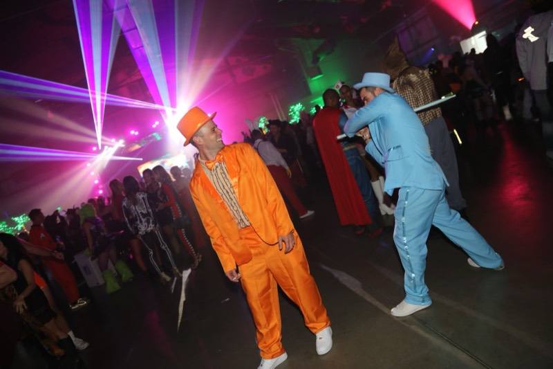 Orange and blue tuxedos grinning beneath the laser canopy at Coloween — Denver Halloween nightlife