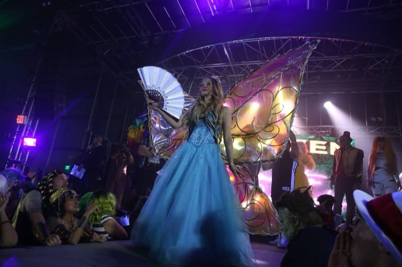 Blue-gown fairy with lit fan and giant iridescent wings on stage at Coloween, Denver's 21+ Halloween party