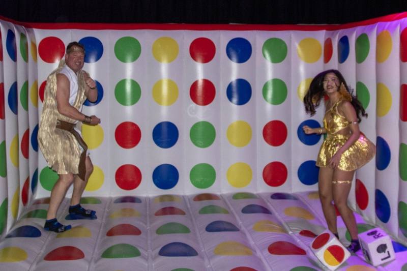 Gold costumes mid-bounce on the giant Twister board, hair airborne at Colorado's biggest adult Halloween party